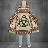A hooded cape with a beige base and Celtic knot patterns in red and green, shown from the back on a child wearing light blue jeans and white sneakers against a white background.
