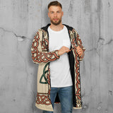 A man wearing a long hooded cardigan with a beige base and intricate red, black, and green Celtic knot patterns, layered over a white t-shirt and blue jeans, against a plain white background.