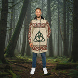 A man wearing a long hooded jacket with a beige base, red Celtic knot patterns, and a green triquetra symbol on the front, paired with blue jeans and white sneakers, against a plain white background.