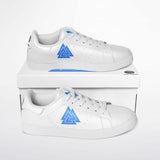 A pair of white low-top sneakers with a blue geometric triangle logo on the side, displayed on top of and in front of a white shoebox against a white background.