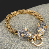 Gold and silver bracelet with wolf head design on a stone surface