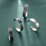 Set of silver cuffs with intricate designs on a green background