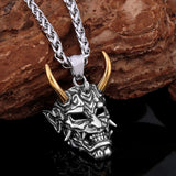 Japanese demon pendant with gold horns on a chain against a stone background