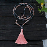 Mala necklace with pink tassel on a dark wooden surface