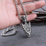 Silver necklace with an arrowhead pendant held by a hand on a dark surface.