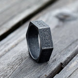 Black ring with engraved text on a wooden surface