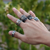 Hand wearing multiple silver rings with a blurred green background