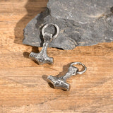 Two silver hammer-shaped charms on a wooden surface with a stone background