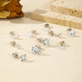 Silver stud earrings with clear gemstones on a beige surface