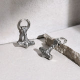 Two silver Thor's hammer charms on a light stone surface