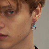 Close-up of a person wearing a silver earring with a turquoise gemstone on a neutral background