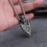 Silver pendant with intricate design held by a hand on a dark surface