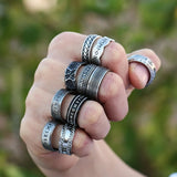 Hand wearing multiple silver rings with a blurred green background