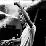 Black and white photo of a DJ at a music event with smoke and equipment.