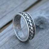 Silver ring with braided design on a wooden surface
