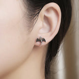 Close-up of an ear wearing a bat-shaped earring with a blurred background