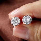Diamond stud earrings held between fingers against a neutral background