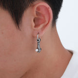Close-up of an ear wearing a silver hoop earring with a small round charm.