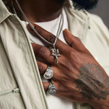 Close-up of a person's hand with silver jewelry and a tattoo on a neutral background