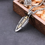 Silver and gold spear pendant necklace on a dark surface with wooden box in the background