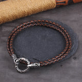 Brown braided leather bracelet with silver clasp on a dark surface