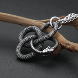 Silver snake-shaped pendant on a branch against a dark background