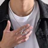 Person wearing a silver necklace with a triangular pendant, holding it with their hand.