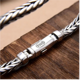 Silver braided bracelet with a clasp on a wooden surface