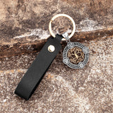 Keychain with black leather strap and decorative pendant on a textured surface