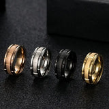 Four metallic rings in gold, silver, black, and rose gold on a dark textured surface.