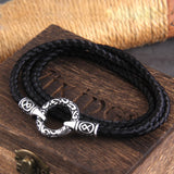Black braided cord bracelet with silver clasp on a wooden surface