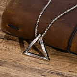 Silver triangle pendant necklace on a wooden surface with a brown leather roll in the background