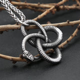 Silver snake pendant necklace on a dark surface with branches