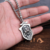 Silver necklace with a detailed pendant held in a hand on a wooden surface