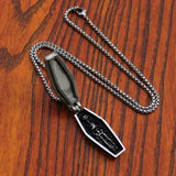 Coffin-shaped pendant on a chain against a wooden background