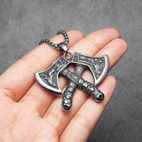 Silver double axe pendant held in a hand against a gray background
