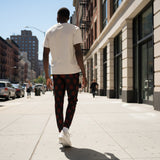 A man wearing black jogger-style pants with a repeating red circular viking symbol pattern, standing on a U.S street