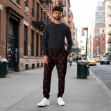 A man wearing black jogger-style pants with a repeating red circular viking symbol pattern, standing on a street