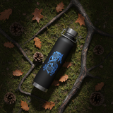 Black water bottle with blue design on a forest floor with leaves and pine cones.