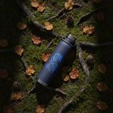 Blue thermos bottle with a tiger design on a forest floor with moss and leaves